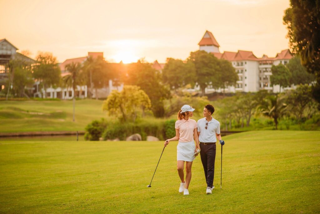 Wide shot of asian chinese smiling young couple golfer holding hand and walking together at golf course